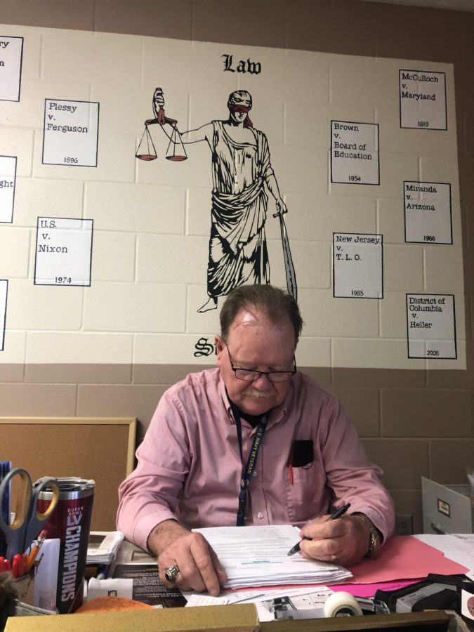 Mr. Black sits at his desk,  grading papers to give back to his students. 