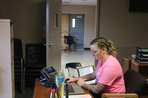 Ms. Sarah Wells (FAC) sits at her temporary desk in the morning, while construction is happening in the next room due to the new fence going up.
