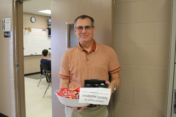 Mr. Siemion (FAC) stands outside his room with a collection box and a bowl of candy to incentivize students who donate to the Pennies for Patients charity.